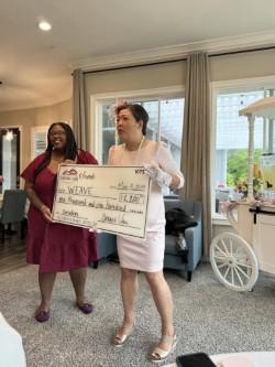 WEAVE Philanthropy Coordinator Alyssa Saunders and Connie Van hold large check for $1,100 to support WEAVE.